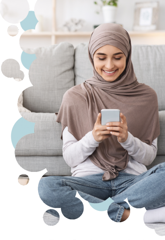 Junge Muslima sitzt mit einem Smartphone vor ihrer Couch